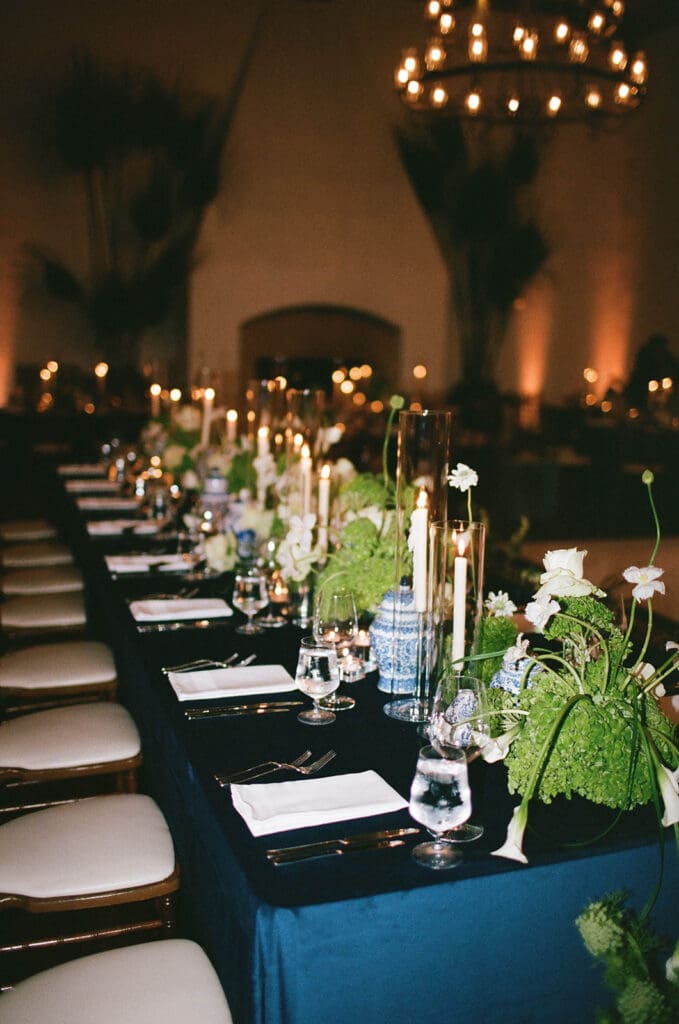 Romantic wedding reception table at Montecito Club in Santa Barbara, styled with navy linens, candlelight, lush green and white floral arrangements, and chinoiserie vases.