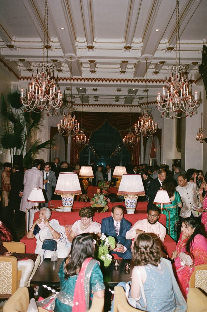 Guests mingling in the grand lounge at Montecito Club in Santa Barbara, with crystal chandeliers, red velvet drapery, and elegant décor creating a luxurious wedding reception atmosphere.