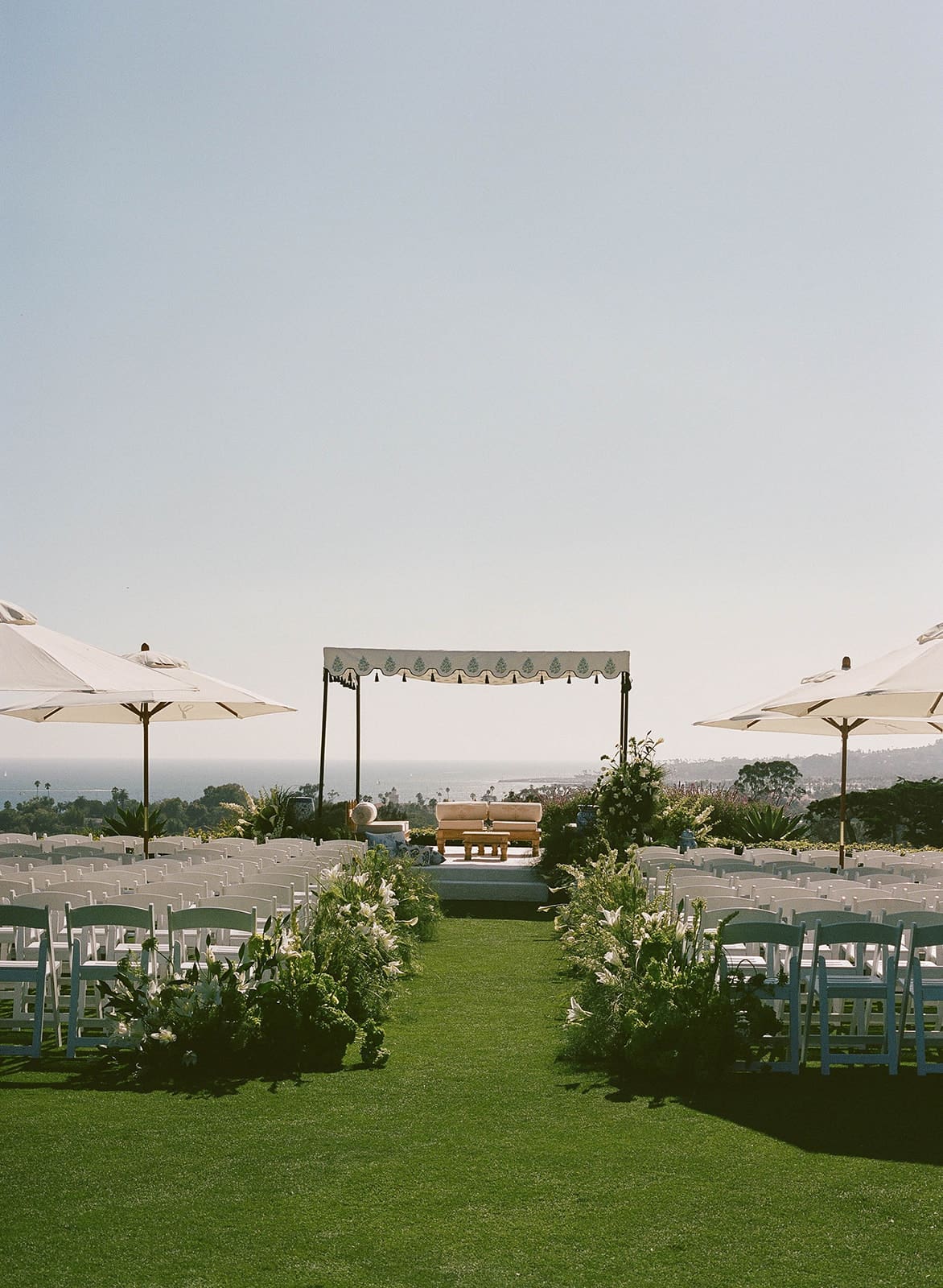 Outdoor wedding ceremony setup at Montecito Club in Santa Barbara, with white chairs, lush floral arrangements, and an elegant canopy overlooking the Pacific Ocean.